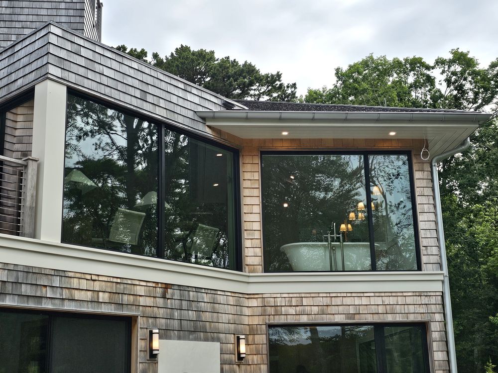 Cedar-shingled coastal home with large filmed picture windows reflecting surrounding trees