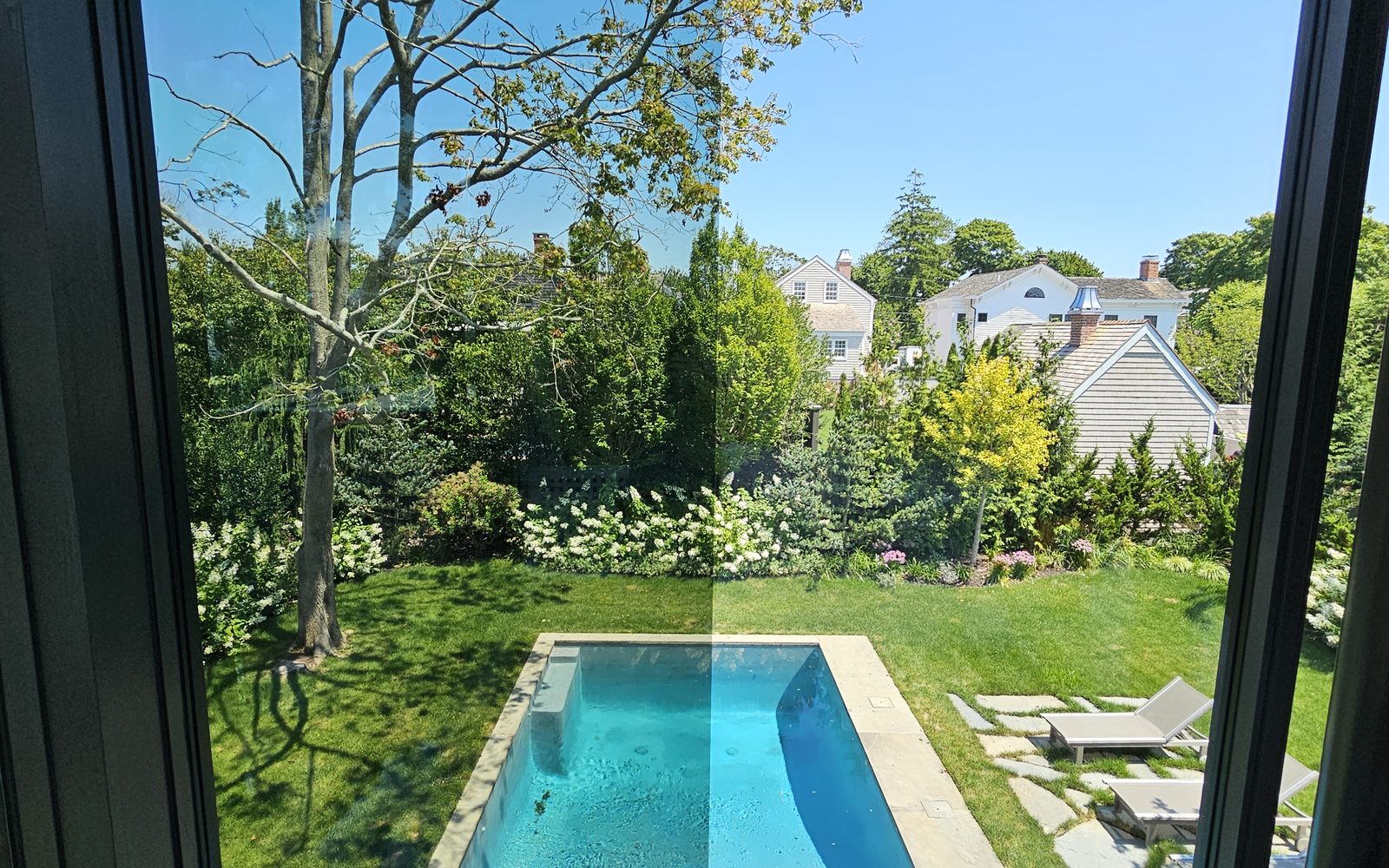 View from inside a Pellikal client's home through filmed glass to a pool and garden, with the view clearly preserved