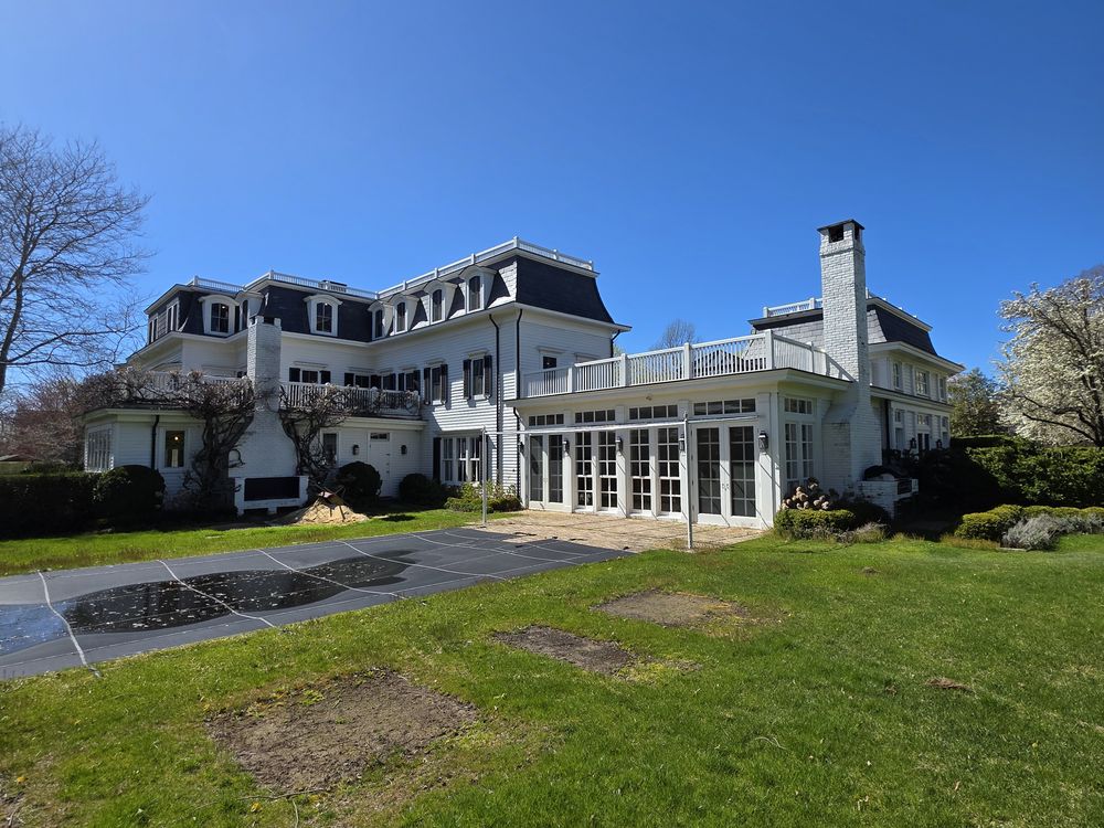 White estate home with a glazed sunroom addition seen across the lawn