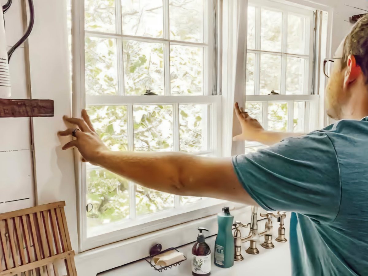 A person fitting a window insert into a kitchen window opening above a sink